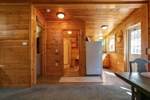 A wooden cabin interior with a kitchen area, a dining table, and a refrigerator. - Pine Ridge Cabin: an all-seasons Wellsboro getaway (Charleston Township)