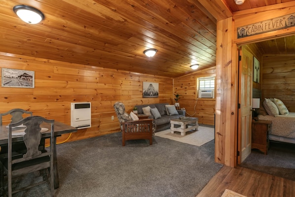 A cabin interior with wooden walls, a sofa, a chair, a table, and a sign reading "CABIN FEVER". - Pine Ridge Cabin: an all-seasons Wellsboro getaway (Charleston Township)
