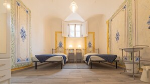 A room with two beds, a chandelier, a window, and a decorative wall panel.