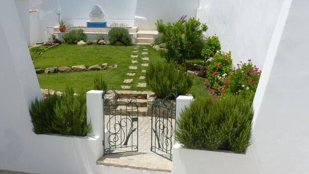 A narrow, white-walled pathway leading to a building with a blue door.