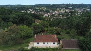 A single-story house with a tiled roof, surrounded by lush greenery and a view of a town in the distance.