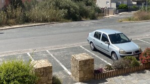 Een parkeerplaats met een witte auto, stenen paaltjes en een rij planten.