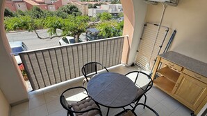 Een balkon met een tafel en stoelen, uitzicht op bergen en een kitchenette met kasten en een ventilator.