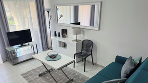 Een moderne woonkamer met een televisie, een glazen salontafel, een zwarte stoel, een blauwgroene bank en een boekenkast.