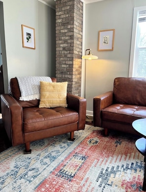 A living room with two brown leather sofas, a patterned rug, a brick pillar, and framed artwork on the walls. - A Design-Led Mountain Lodge ~ 4BR Retreat for Gathering ~ Firepit, Views, Stars (Mars Hill)