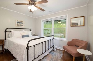A bedroom with a bed, a ceiling fan, a window with a view of the outdoors, a bedside table, and a chair. - Mountain Getaway | Fire Pit, Mtn Scenery, Stars (Mars Hill)