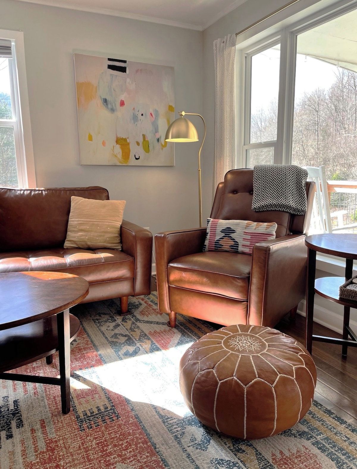 A modern living room with a brown leather sofa, a brown leather armchair, a round coffee table, and a patterned rug.
