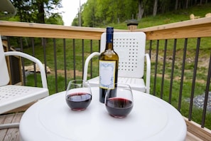 A deck with a table, two chairs, a bottle of wine, and two glasses of red wine.