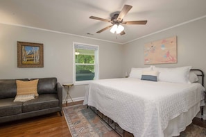 A bedroom with a bed, a gray sofa, a ceiling fan, a window, and artwork on the walls. - Mountain Getaway | Fire Pit, Mtn Scenery, Stars (Mars Hill)