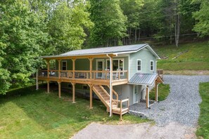 A two-story house with a covered porch and a small deck, surrounded by trees and a gravel driveway. - Mountain Getaway | Fire Pit, Mtn Scenery, Stars (Mars Hill)