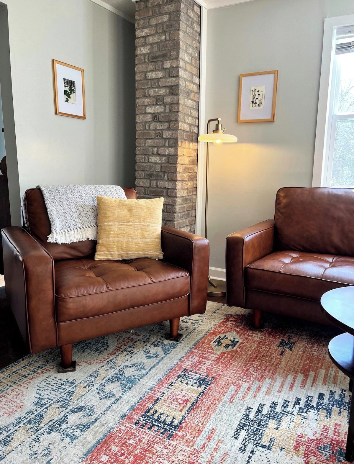 A living room with two leather sofas, a patterned rug, a brick pillar, and framed artwork on the walls.