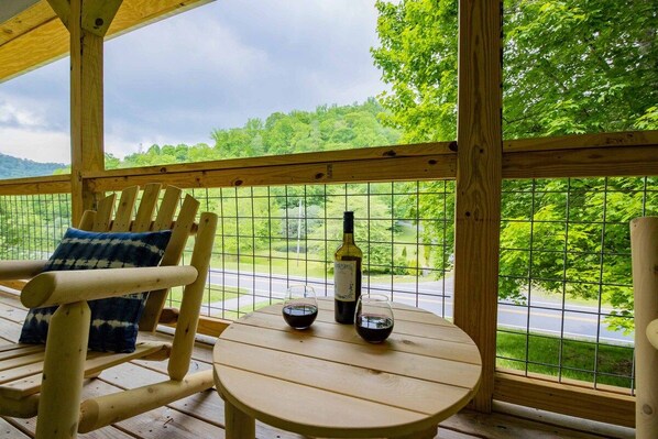 A wooden deck with a table and chairs, a bottle of wine, and a glass.