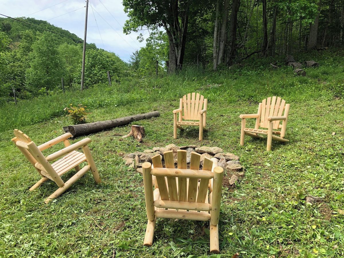 Three wooden Adirondack chairs arranged around a fire pit in a grassy outdoor setting.
