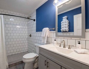 Un baño moderno con paredes de azulejos blancos, una pared de acento azul, una ducha con puerta de cristal, un inodoro, un lavabo con espejo y un perchero para toallas.