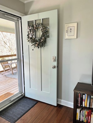 A white door with a wreath, a doormat, a bookshelf, and a light switch on the wall. - Mountain Getaway | Fire Pit, Mtn Scenery, Stars (Mars Hill)