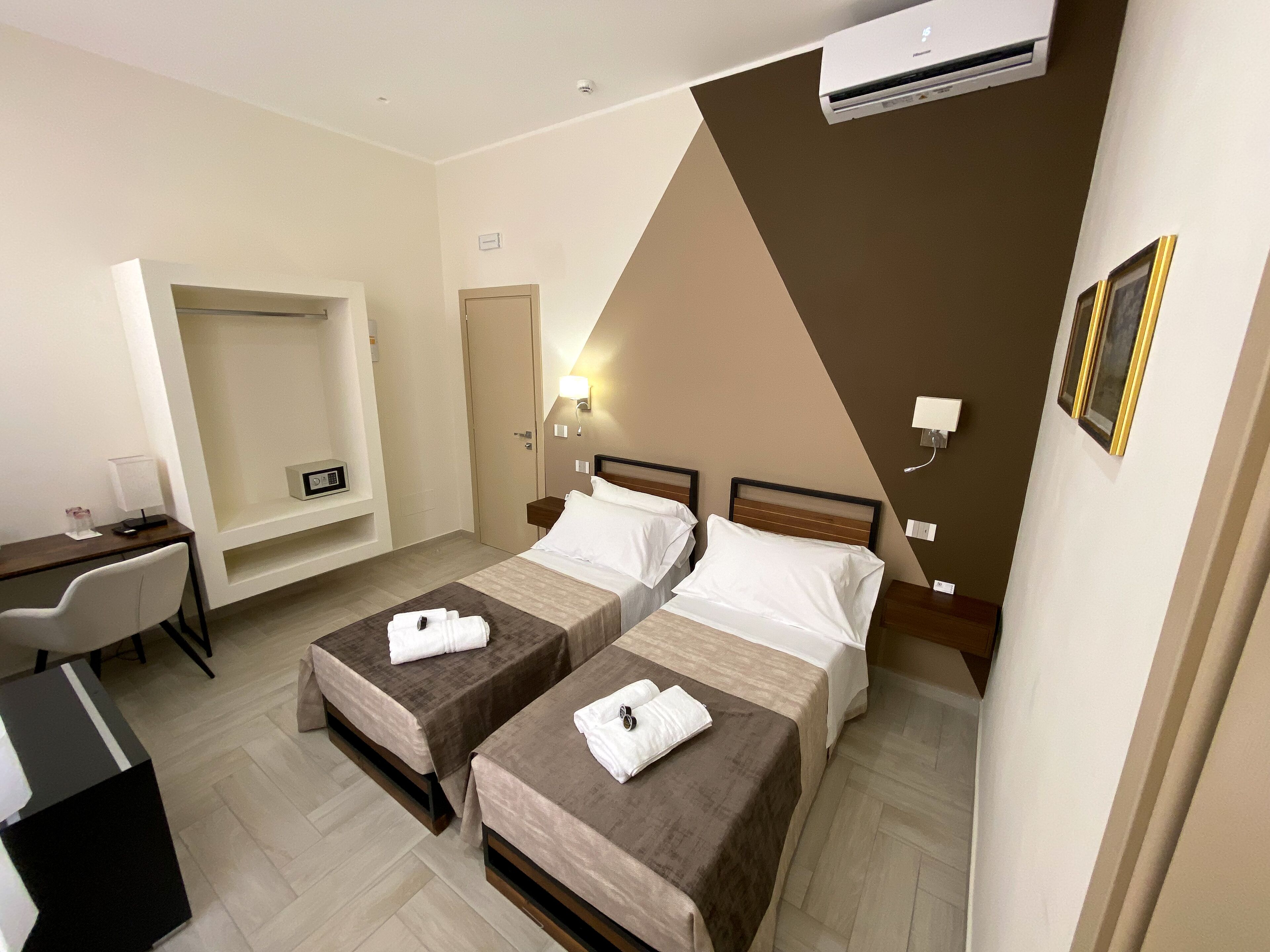 A hotel room with two beds, a desk, a chair, and a small seating area.