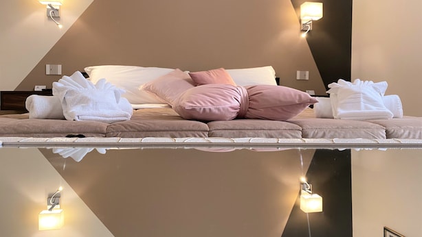 Habitación de hotel con cama, almohadas y toallas. Cuenta con luces fijadas en la pared y un cuadro enmarcado.