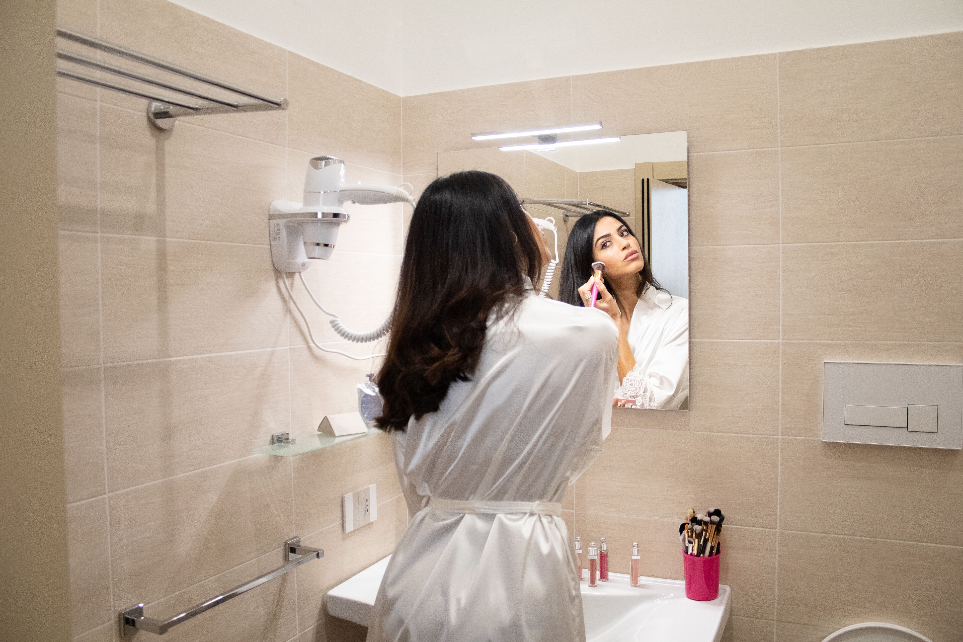 A bathroom with a sink, mirror, towel rack, and a pink container with toiletries.