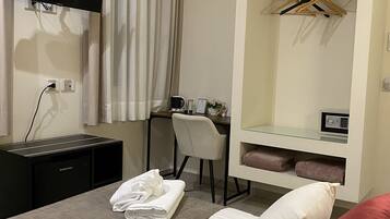 Habitación de hotel con cama, escritorio, silla, televisor montado en la pared y armario con espejo.