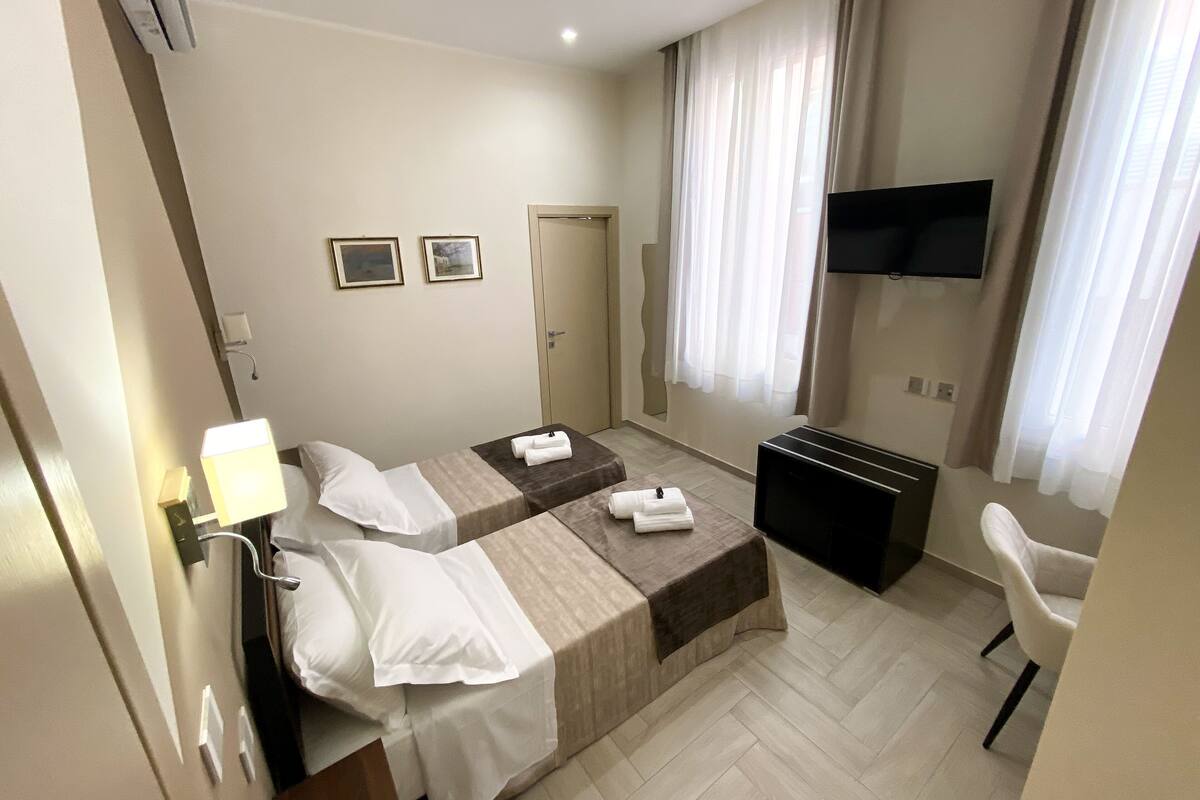 A hotel room with two beds, a TV, a desk, and a chair.