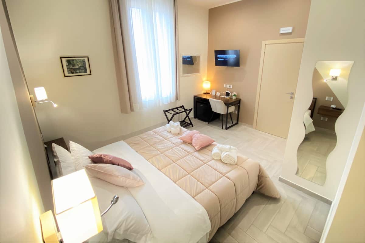 A hotel room with a bed, a desk, a chair, a TV, and a bathroom mirror.