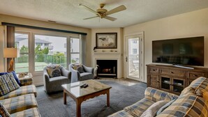 A living room with a fireplace, a television, and a ceiling fan. - Cordgrass Bay 2315-E (Wrightsville Beach)