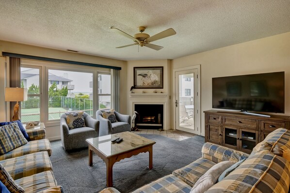 A living room with a fireplace, a television, and a ceiling fan.