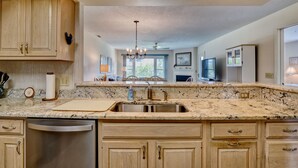 A kitchen with granite countertops, stainless steel appliances, wooden cabinets, and a chandelier. - Cordgrass Bay 2315-E (Wrightsville Beach)