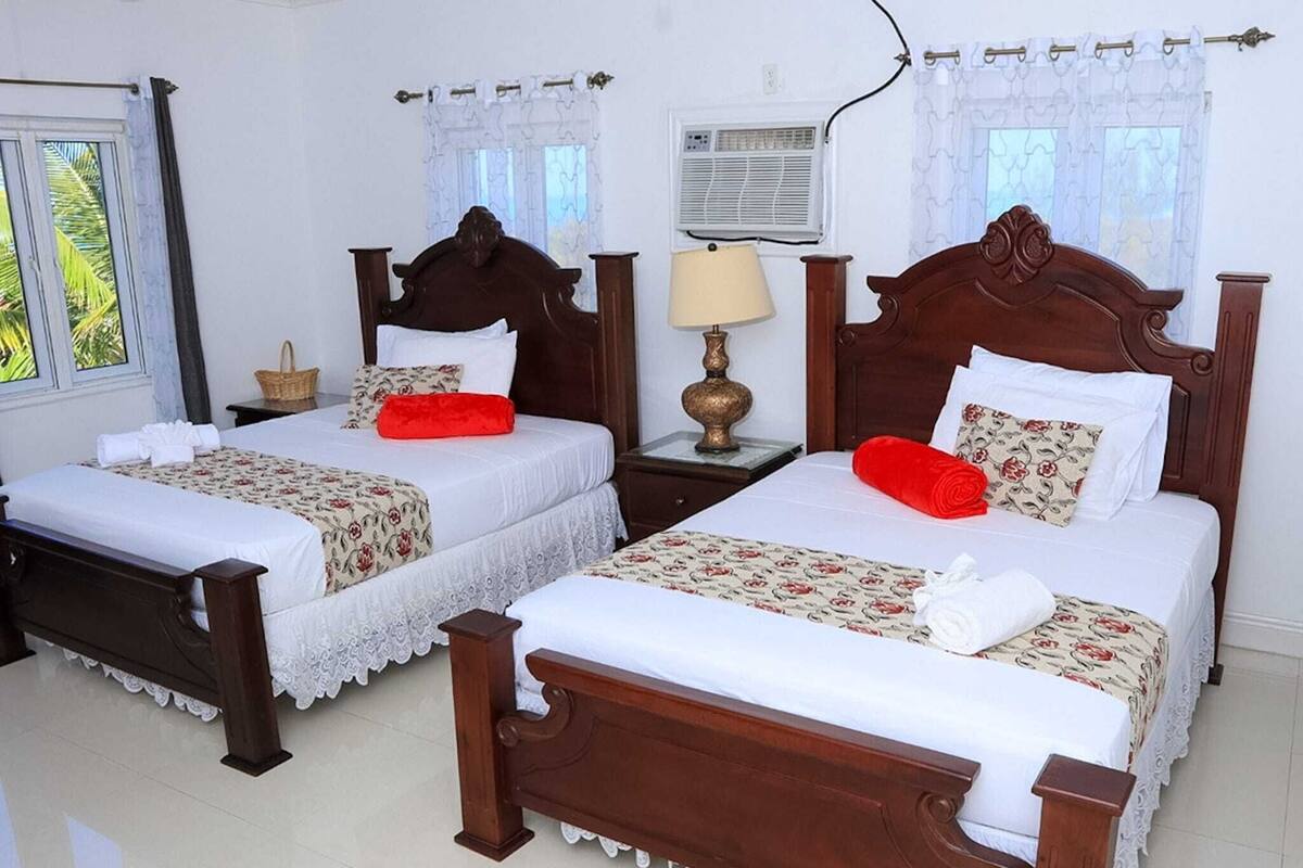 A hotel room with two wooden beds, white linens, floral-patterned bedspreads, and a small bedside table with a lamp.