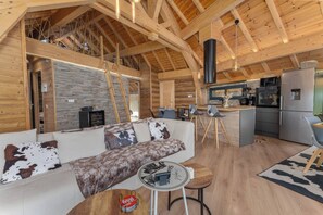 A cozy cabin interior with a sofa, dining area, kitchen, and a loft space.