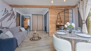 Ein modernes Wohnzimmer mit einer Couch, einem Esstisch für zwei Personen und einer Küche im Hintergrund.