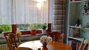 Ein Essbereich mit einem runden Holztisch, vier Stühlen, einer Blumenvase und einem Bücherregal mit Büchern und Dekoration.