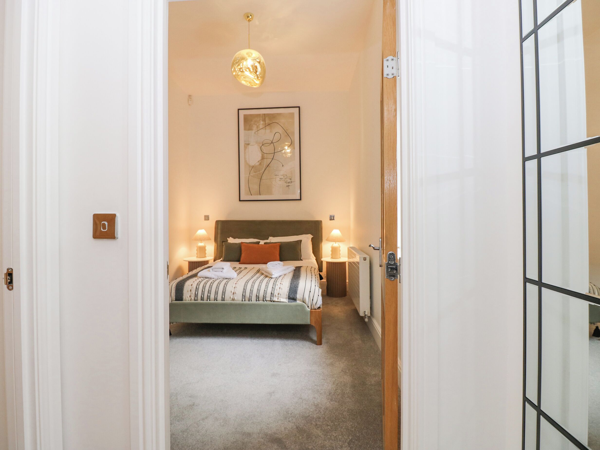 A bedroom with a bed, bedside lamps, a radiator, and a hanging light fixture.