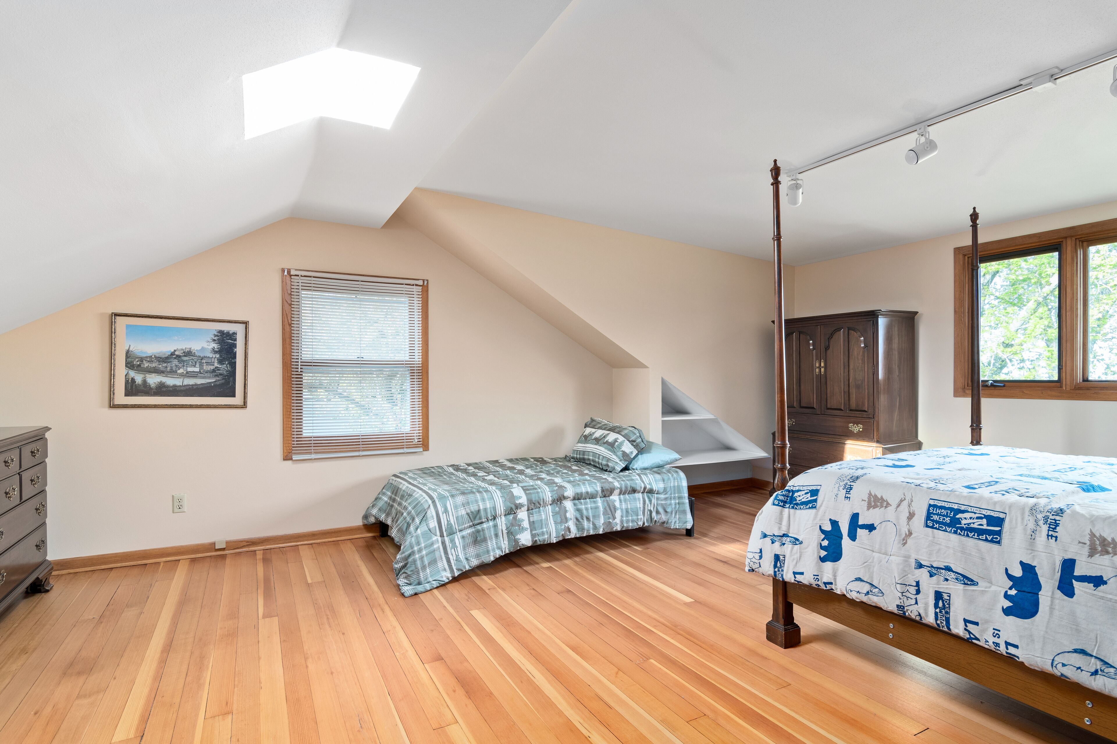 Ein Schlafzimmer mit schrägem Dach, Holzdielen, einem Himmelsbett, einem Schminktisch, einem Nachttisch und einem Fenster mit Jalousien.