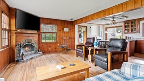 Un salón con suelo de madera, chimenea, sillones de cuero, televisor y zona de comedor.