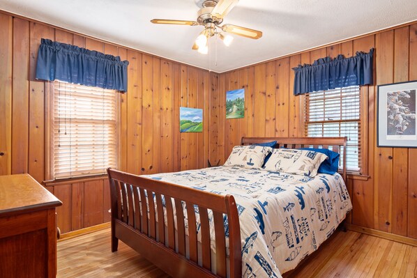 Un dormitorio con paredes y cama de madera, y dos ventanas con cortinas azules.