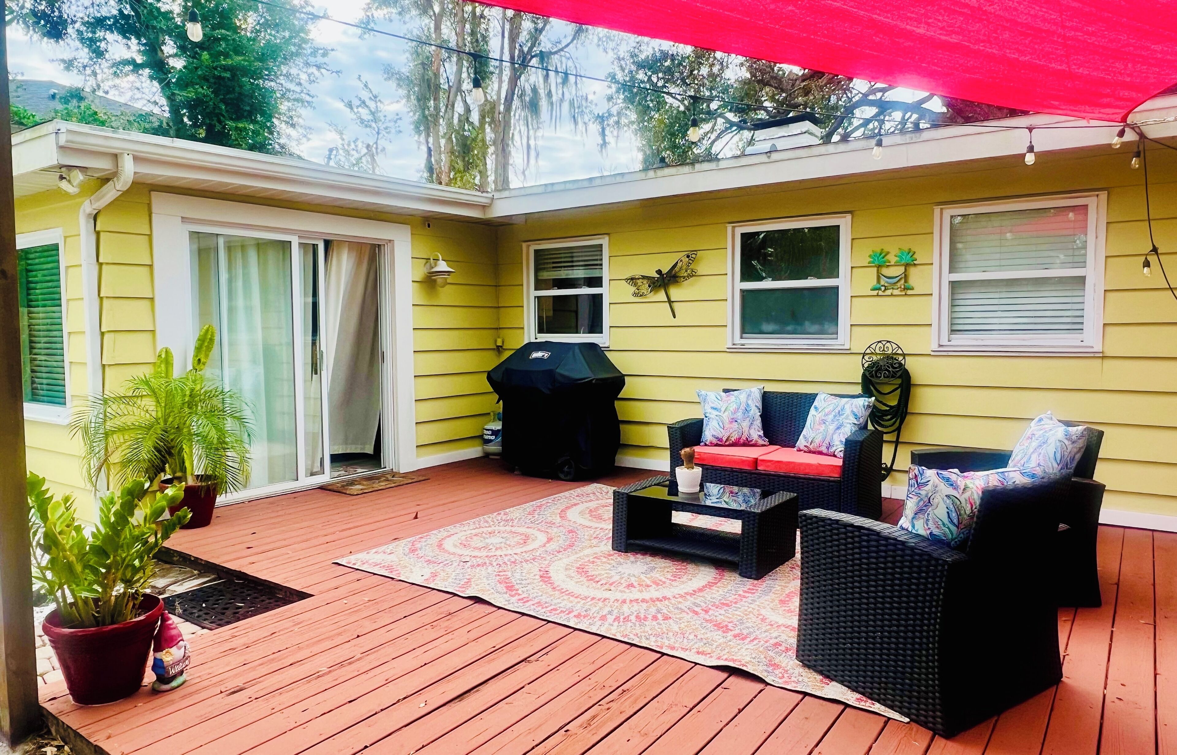 A covered patio with outdoor furniture, a grill, and potted plants.