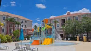 A water park with slides and a pool, surrounded by buildings with balconies and windows.