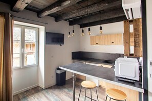 A compact kitchen with a bar area, wooden ceiling beams, and a large window.