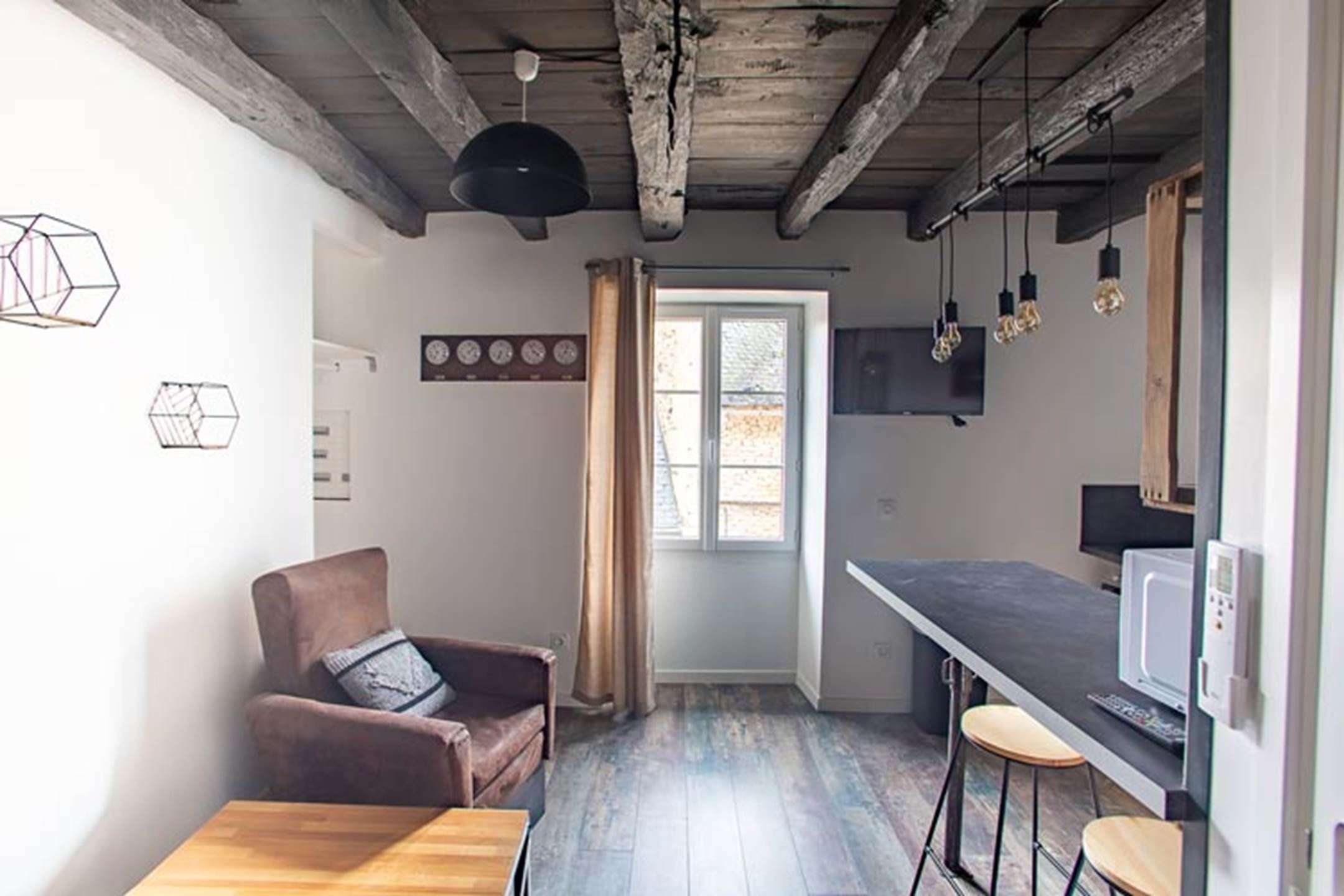 Eine kleine Küche mit Holztisch, Barhocker, Stuhl und einem Fenster mit Vorhängen.