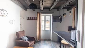 Eine kleine Küche mit Holztisch, Barhocker, Stuhl und einem Fenster mit Vorhängen.