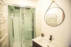 Ein Badezimmer mit einer Duschkabine, einem weißen Waschbecken und einem runden Spiegel an der Wand.