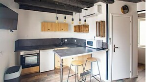 Una cocina moderna con encimera negra, armarios de madera, un microondas y dos taburetes.