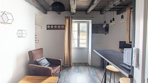 Un espacio habitable compacto con kitchenette, comedor y zona de estar con una silla y una mesa.
