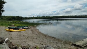 A calm lake with kayaks on the shore, surrounded by trees and a cloudy sky.