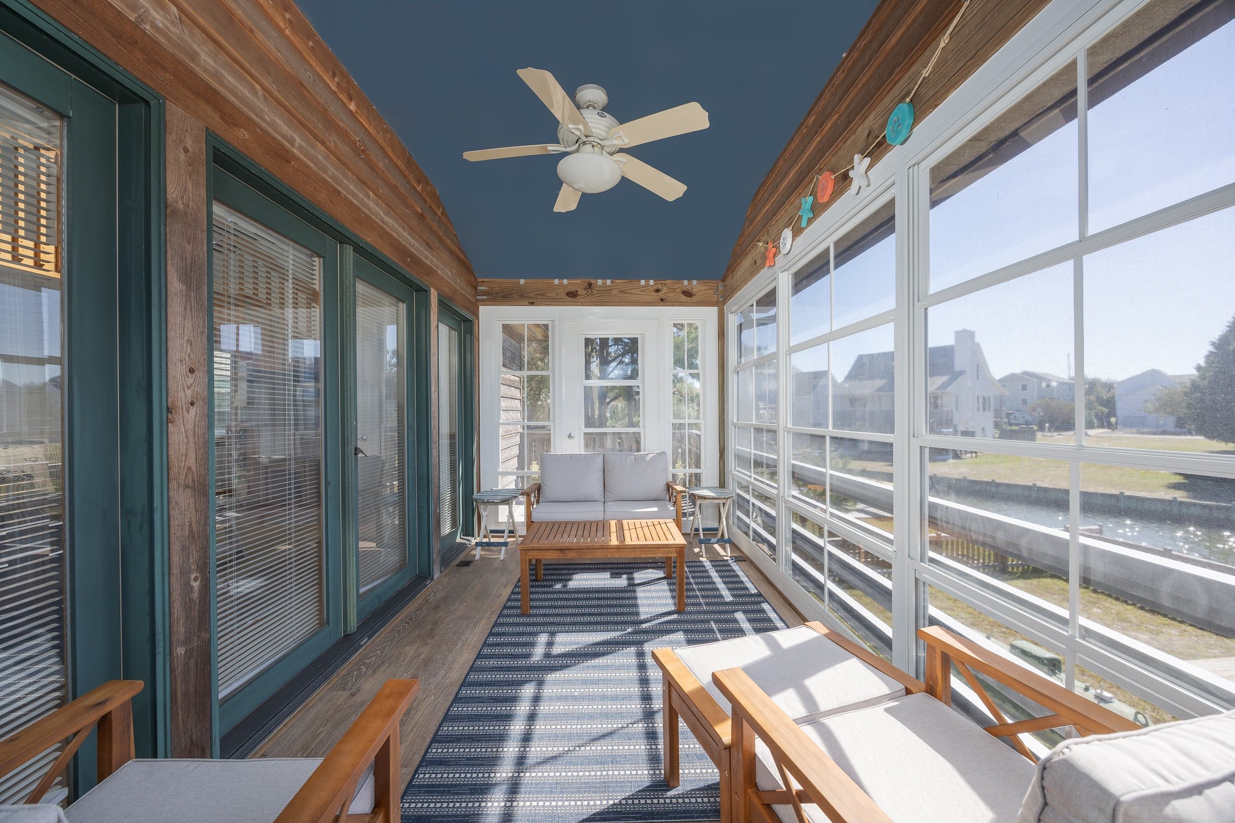A sunroom with a ceiling fan, large windows, and a seating area with a view of the outside.