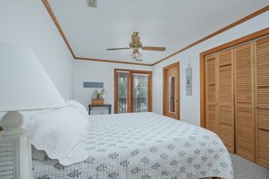 Ein Schlafzimmer mit einem Bett, einem Deckenventilator, einem Fenster mit Jalousien und einem Holzschrank.