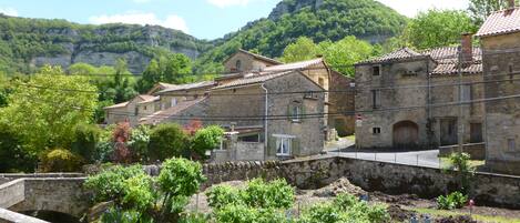 Un bâtiment en pierre, doté d’un toit en tuiles, entouré d’une végétation luxuriante et d’un mur de pierre.