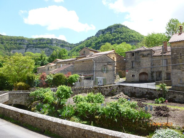 A stone building with a tiled roof, surrounded by lush greenery and a stone wall.