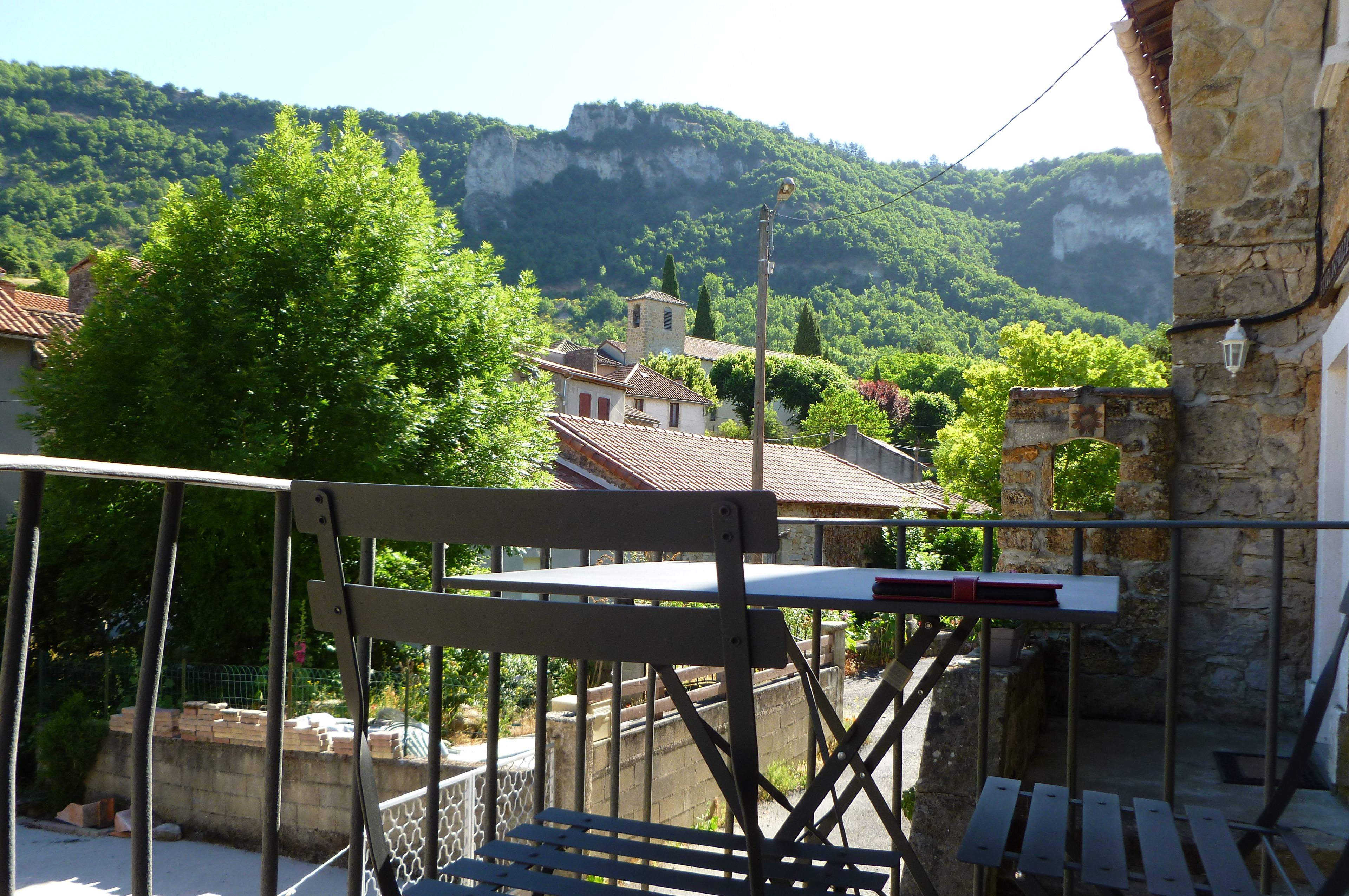 A balcony with a metal railing, overlooking a village with traditional buildings and a mountainous backdrop.